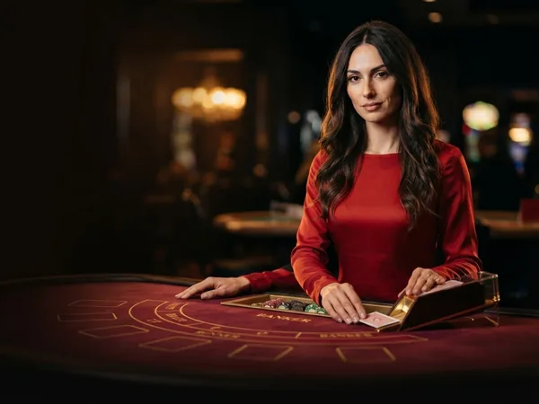 Lobby-style live table card: portrait crop of the croupier dealing from the card shoe at a red table